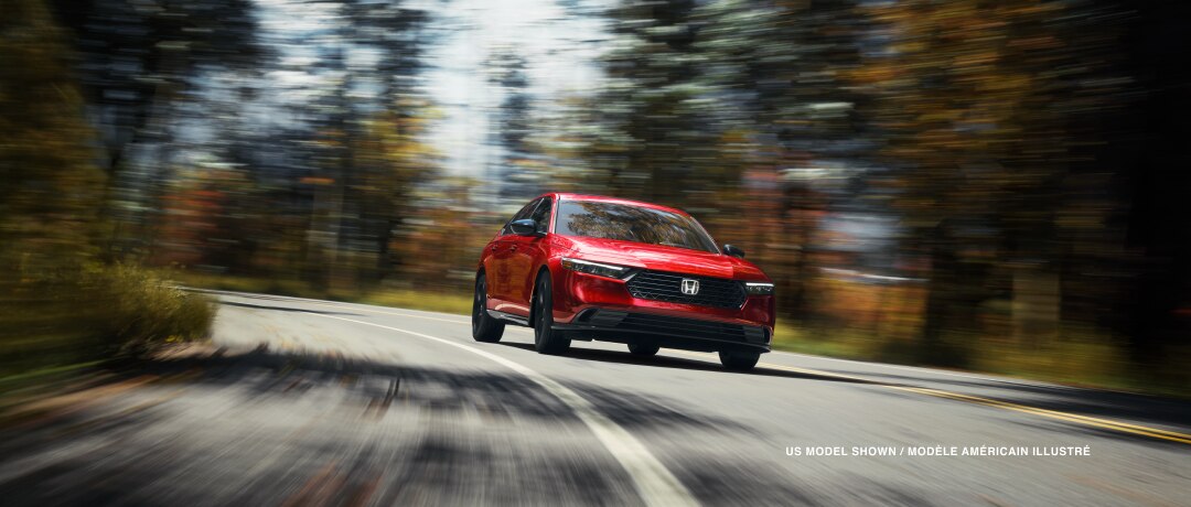 3/4 front view of red Accord, driving toward camera, taking a turn on a temperate rainforest highway in the day.