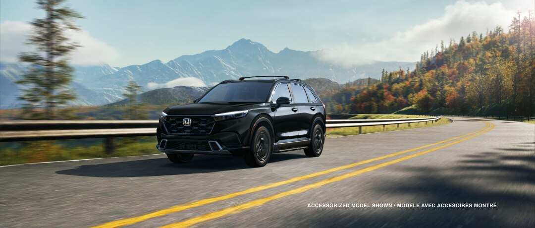 3/4 front view of black CR-V driving on a winding forest highway with fall-coloured trees and mountain range as backdrop. 