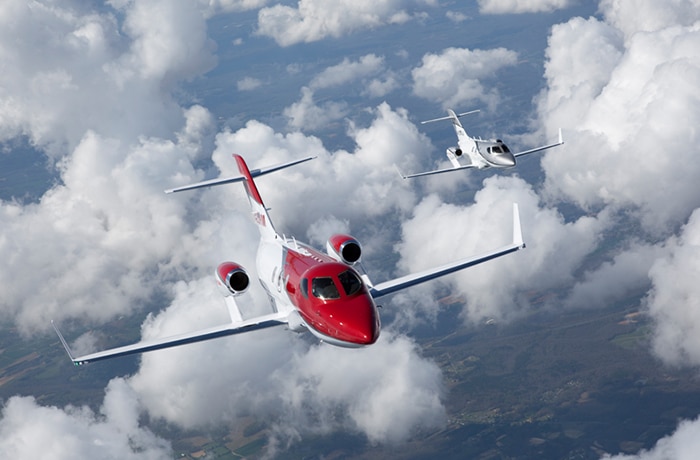 Red and silver Honda Jet flying in the sky.