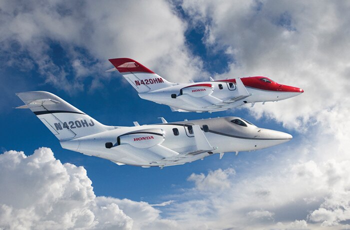 Image of a red and grey Honda jet flying in the sky. 